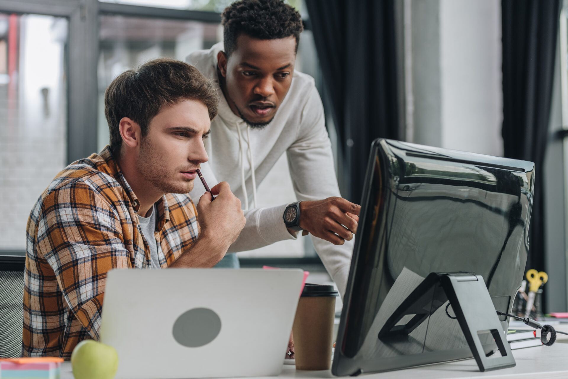 african american programmer pointing at computer monitor near serious colleague